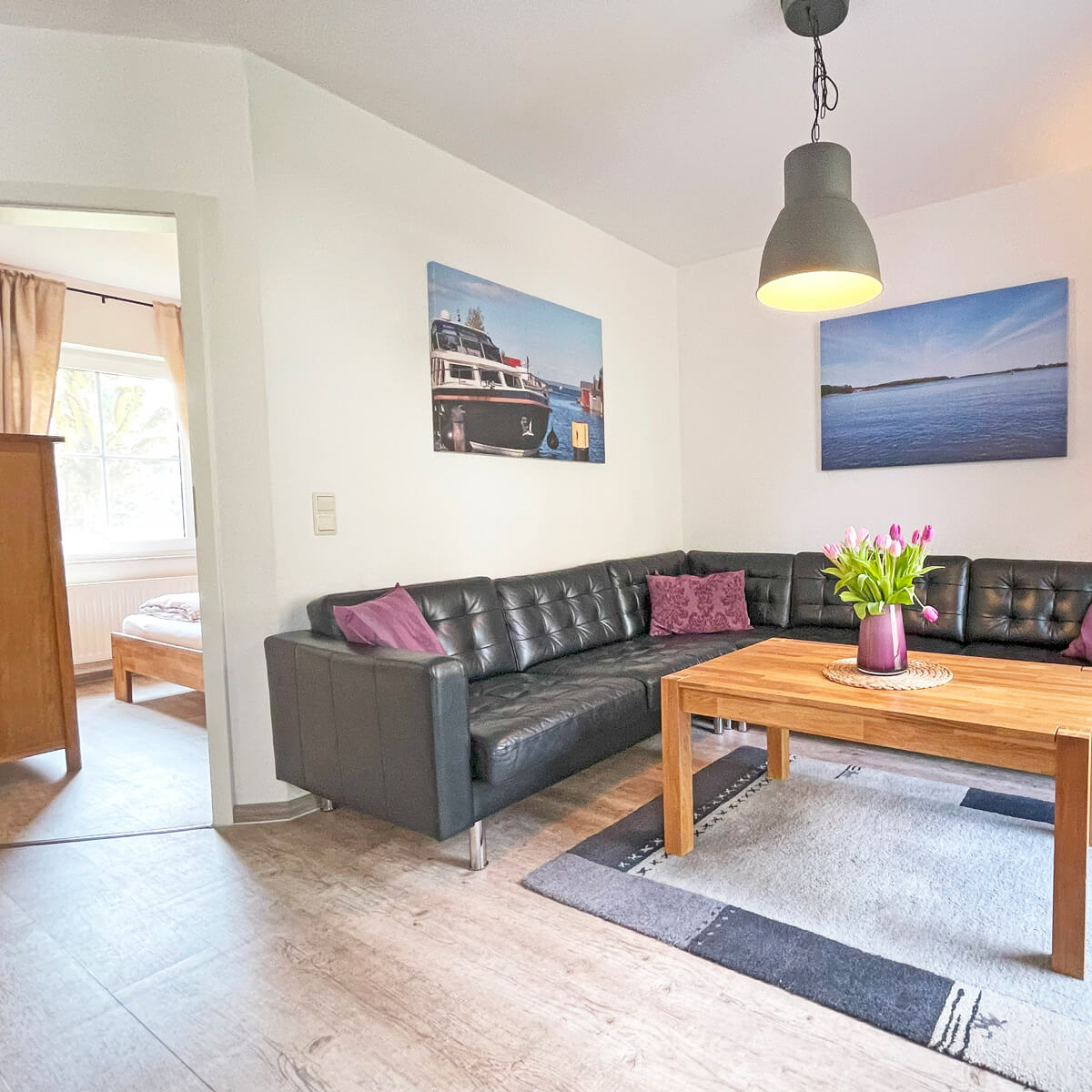 Wohnzimmer im Ferienhaus Fox Lenz mit Ecksofa, Holztisch und Zugang zum Schlafzimmer